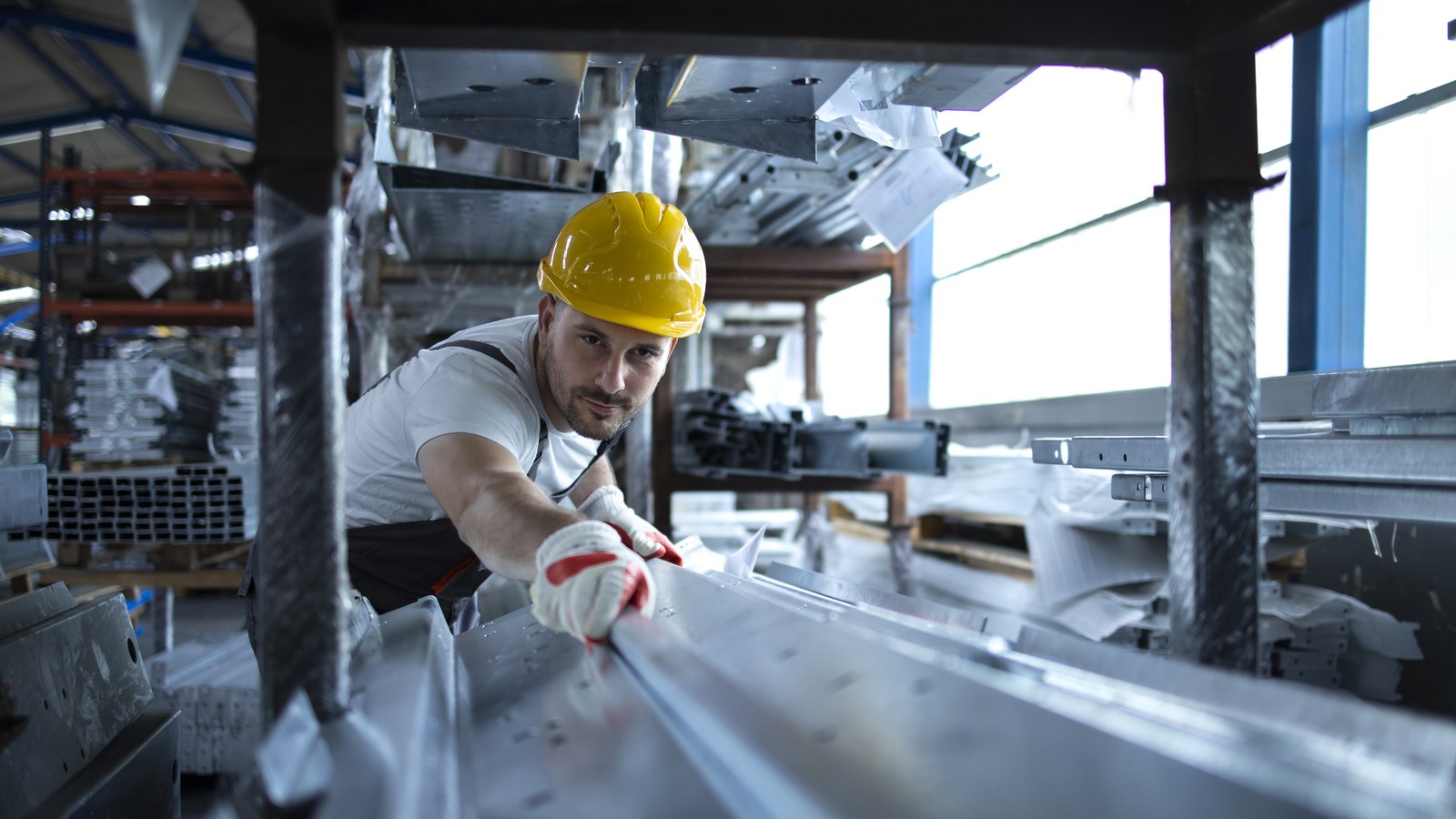 A worker inspecting extruded aluminium profiles in a warehouse
