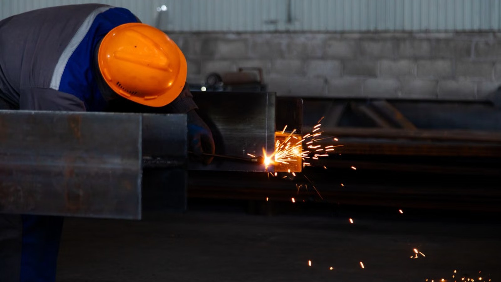 A welder joining structural steel sections in a fabrication workshop