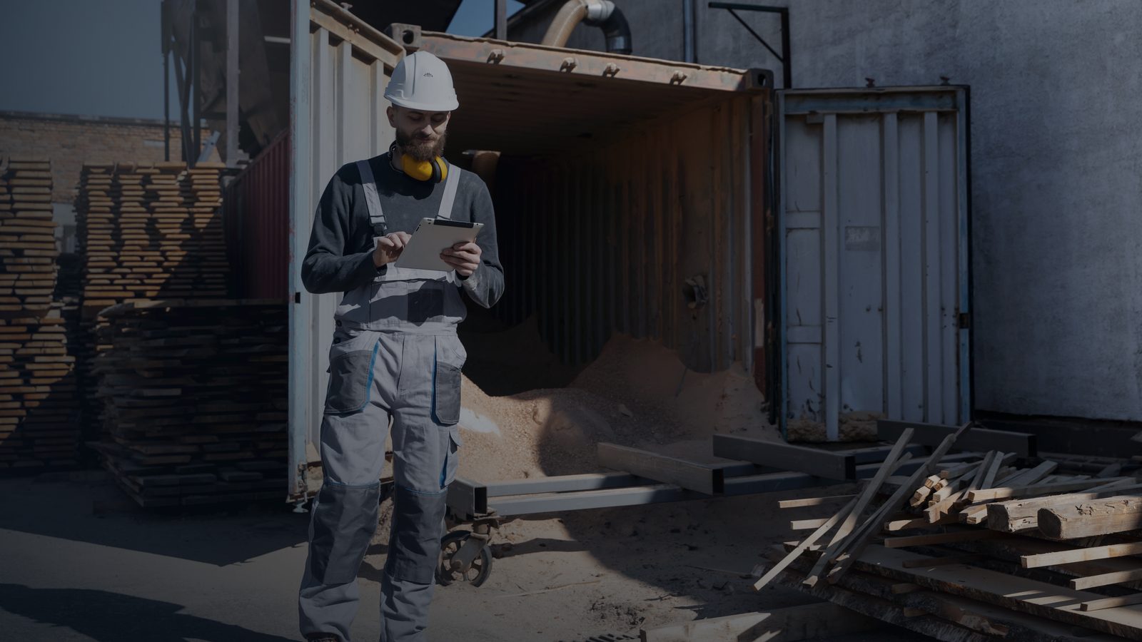 A supplier checking timber stock against a tablet in a sawmill yard